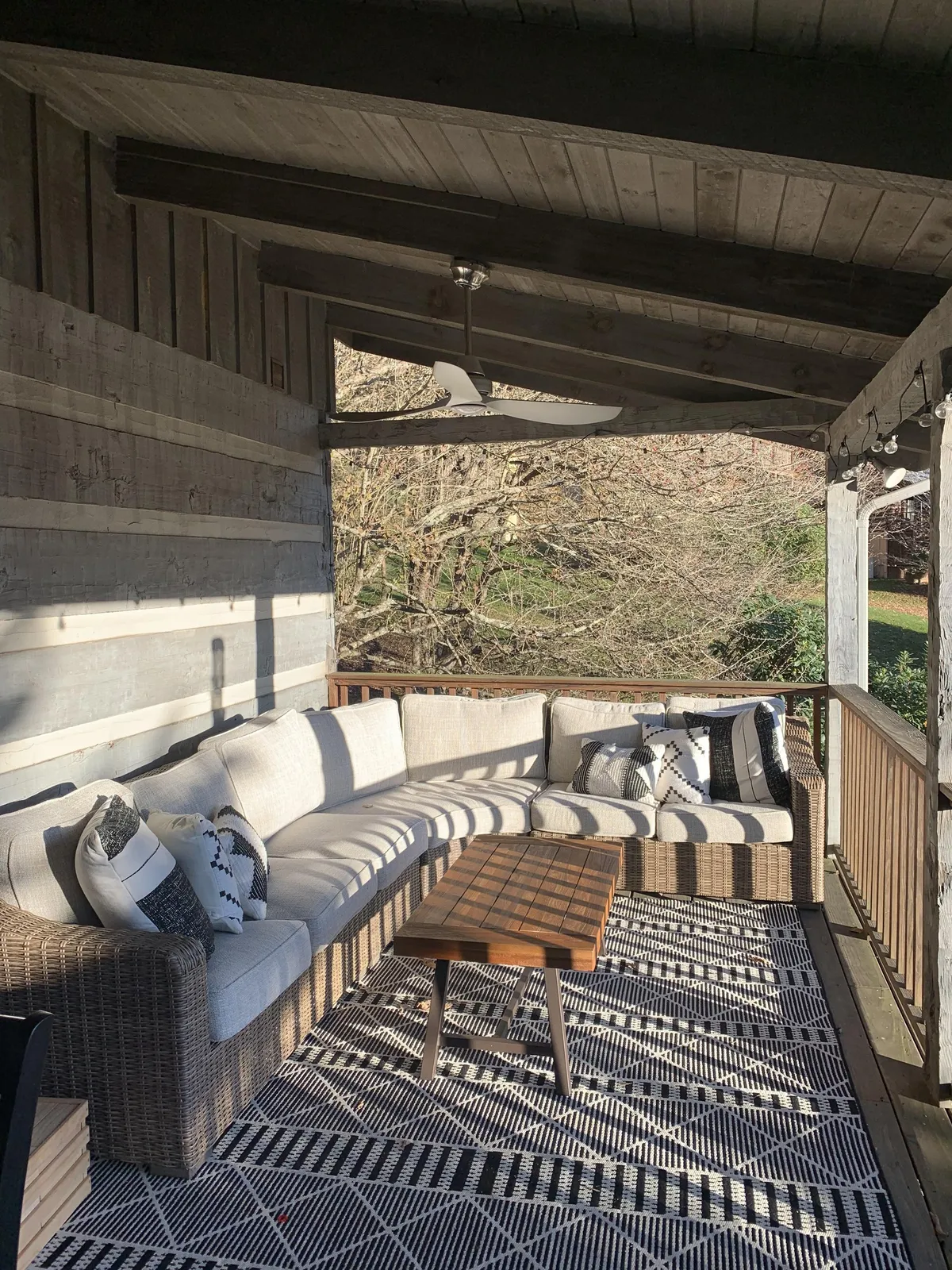 An inviting outdoor sectional sofa and coffee table are arranged on a wooden deck, accented with decorative pillows and an area rug. The setting suggests a space for socializing, relaxing, and enjoying the mountain air at sunrise or sunset.
