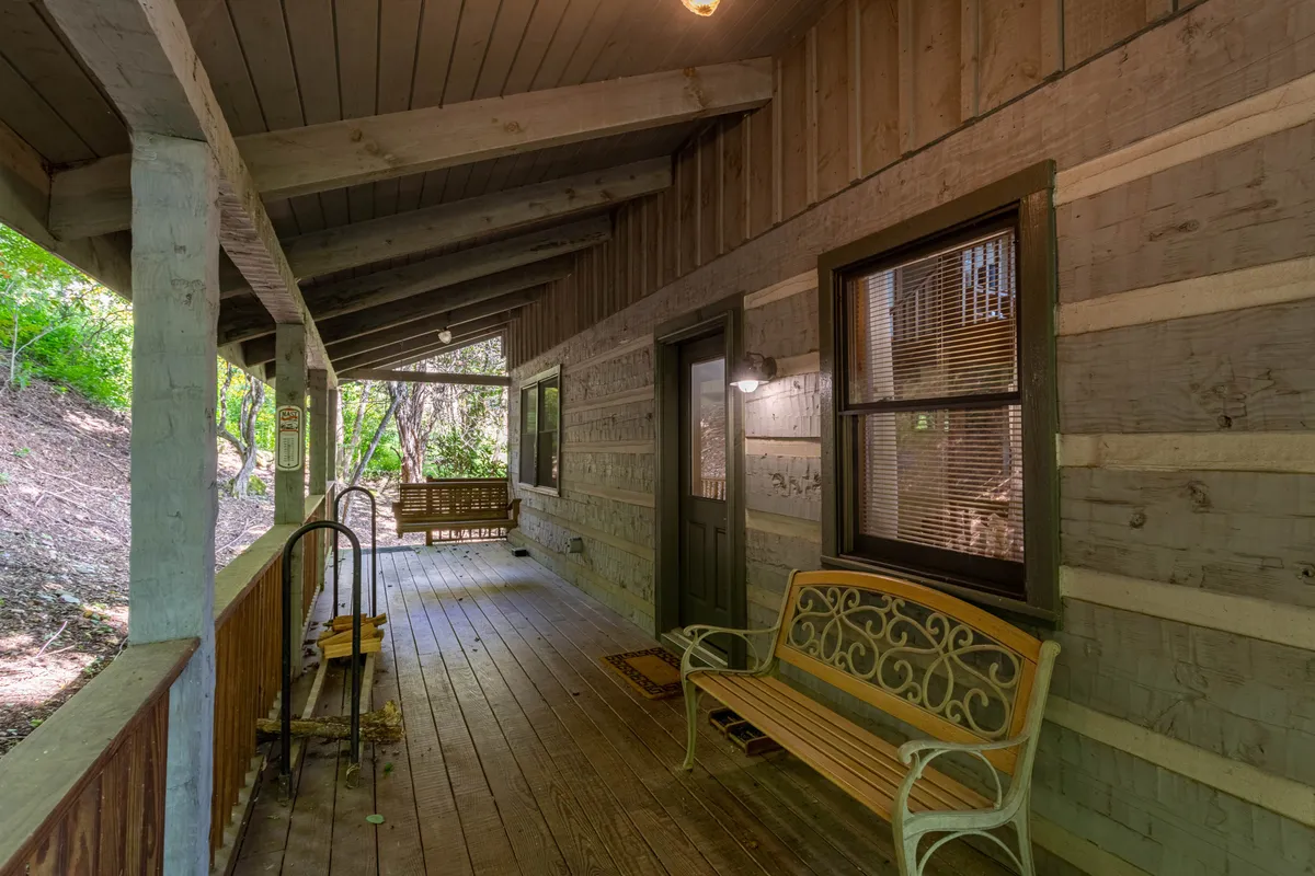 A serene wooden porch with a classic swing and a metal bench invites moments of peaceful contemplation. Surrounded by greenery, the porch swing is perfectly positioned for unwinding, reflecting the cabin's inviting and cozy spirit. The setup suggests both solo relaxation and intimate conversation with loved ones.