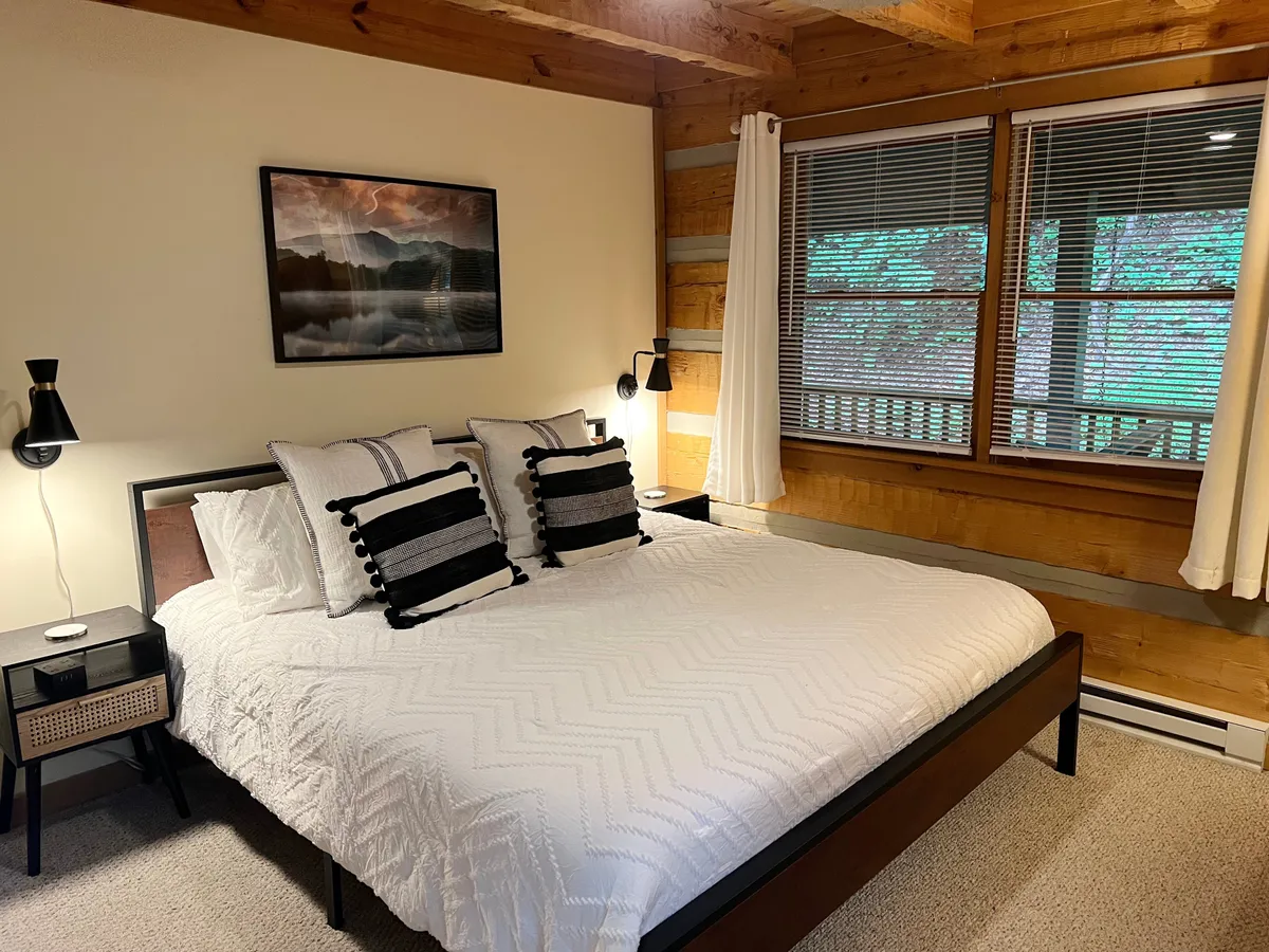 A tranquil bedroom featuring a neatly made bed, a framed picture on the wall, and a window letting in soft natural light. The space is uncluttered and serene, offering a peaceful retreat for rest and relaxation.