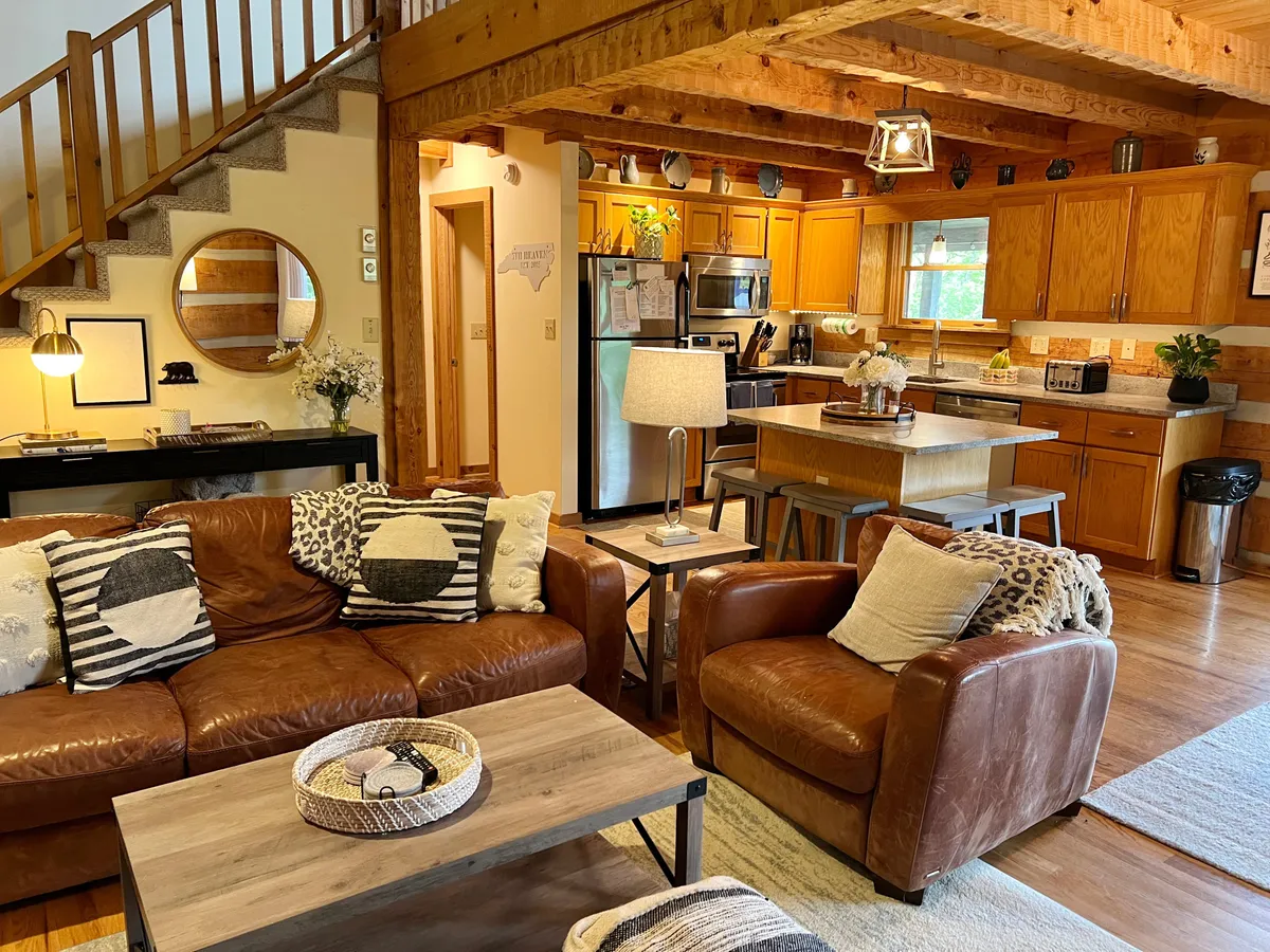 This inviting scene features a spacious open-plan living area with plush leather sofas, a large wooden dining table set for gatherings, a well-appointed kitchen with ample cabinetry, and a staircase hinting at the multi-level layout. Decorative accents and natural light contribute to a cozy, communal atmosphere ideal for family connection.