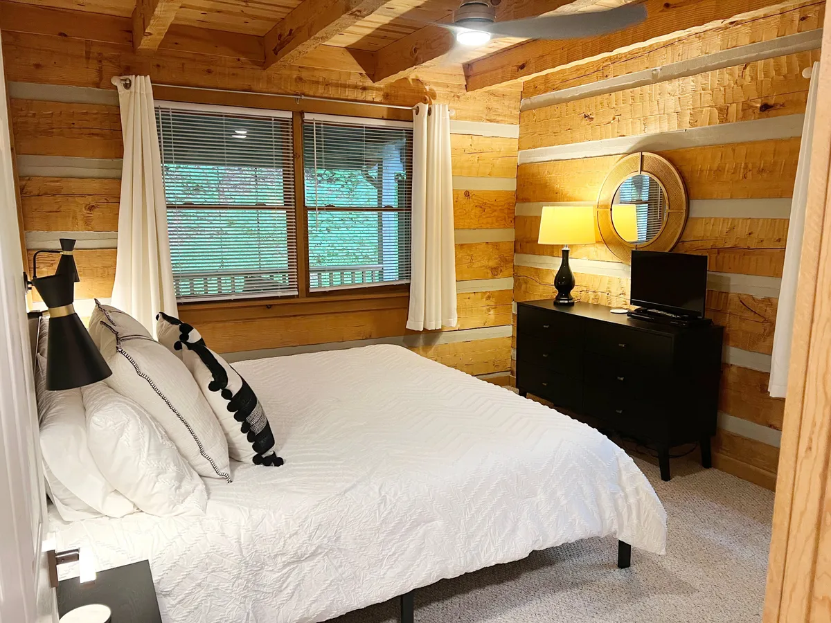 A comfortable bedroom with a large bed, window, lamp, TV, and dresser. The room is bathed in gentle light, inviting guests to relax, read, or unwind while enjoying modern amenities.