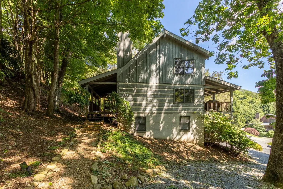 This image captures the unique architectural design of the cabin nestled among lush greenery. The winding path leads toward the welcoming entrance, while the surrounding trees hint at the peaceful, natural setting and nearby trails.